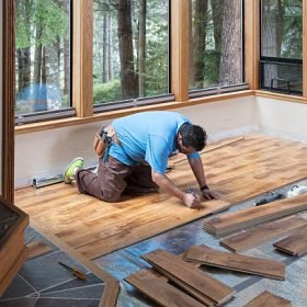 Man installing wood flooring in home.
